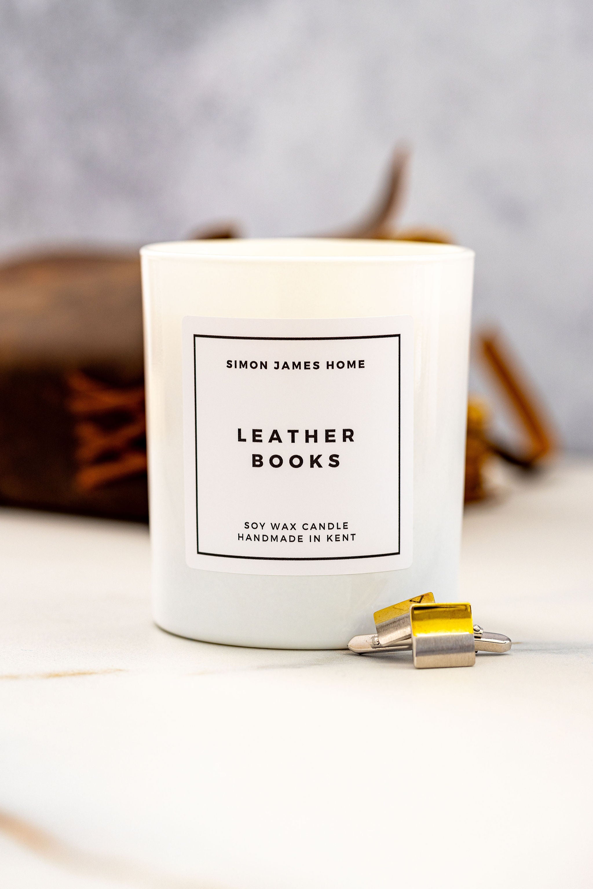 Candle labeled 'Simon James Home Leather Books' on a neutral background