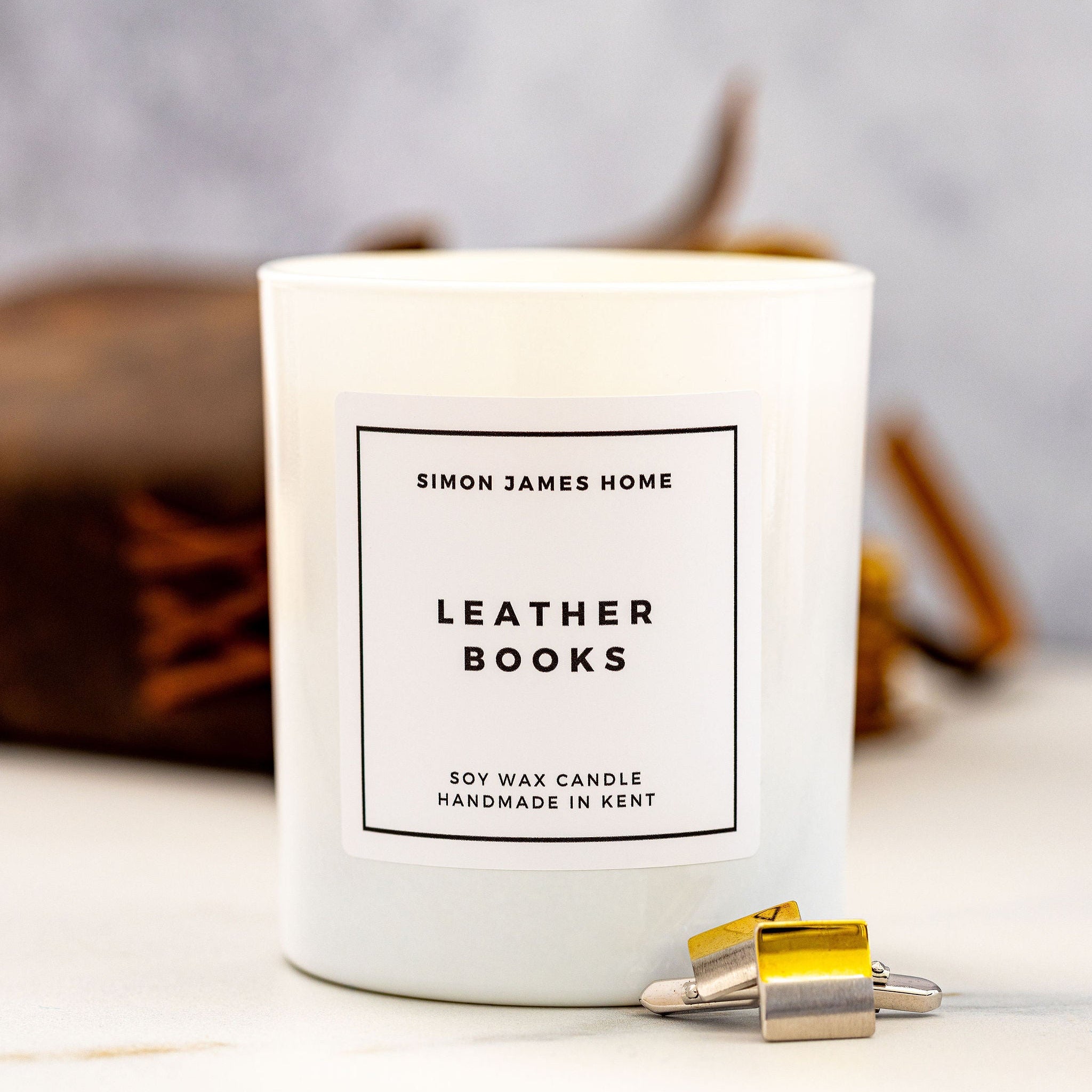 Candle labeled 'Simon James Home Leather Books' on a neutral background