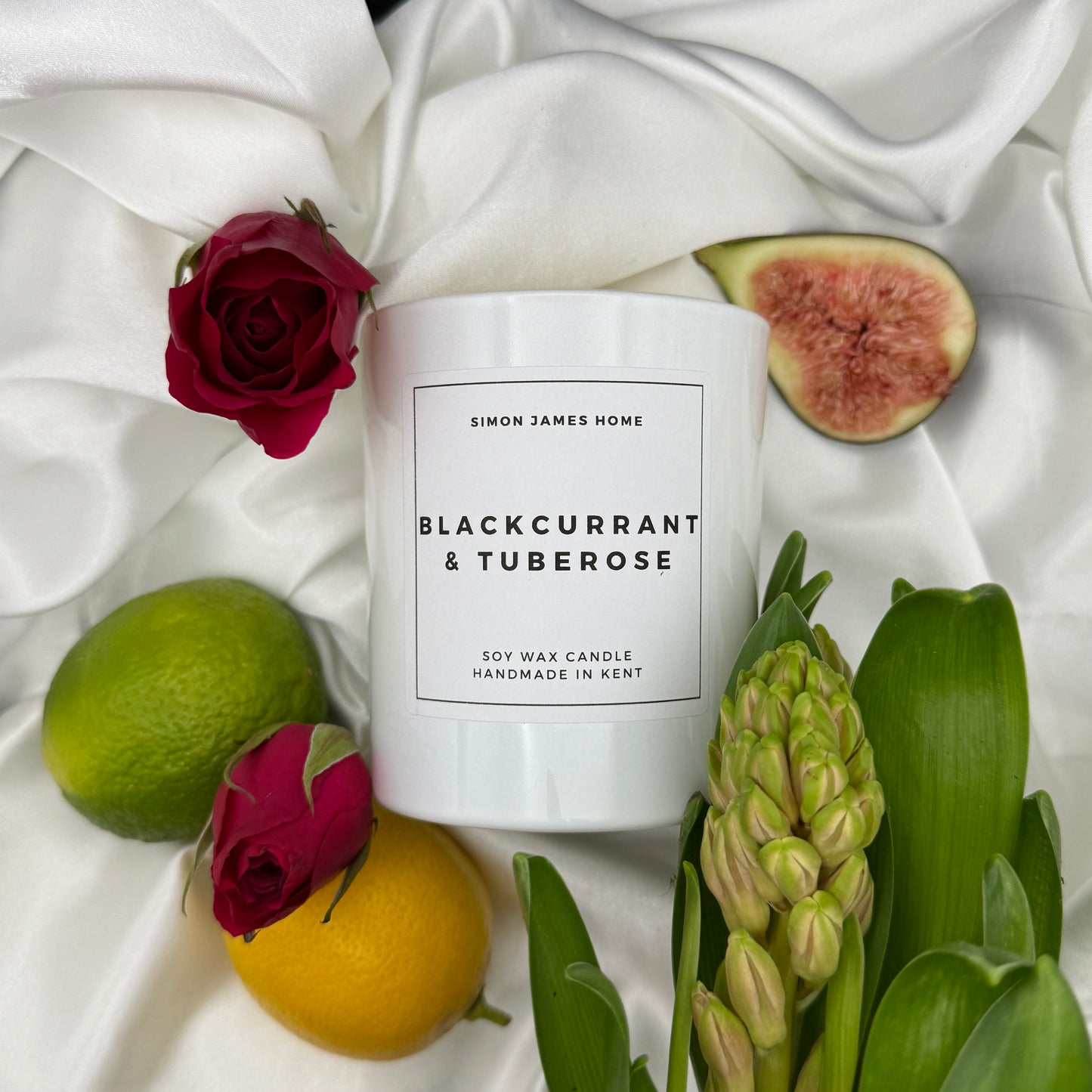 Blackcurrant & Tuberose candle in a white glass jar, surrounded by flowers and fruit