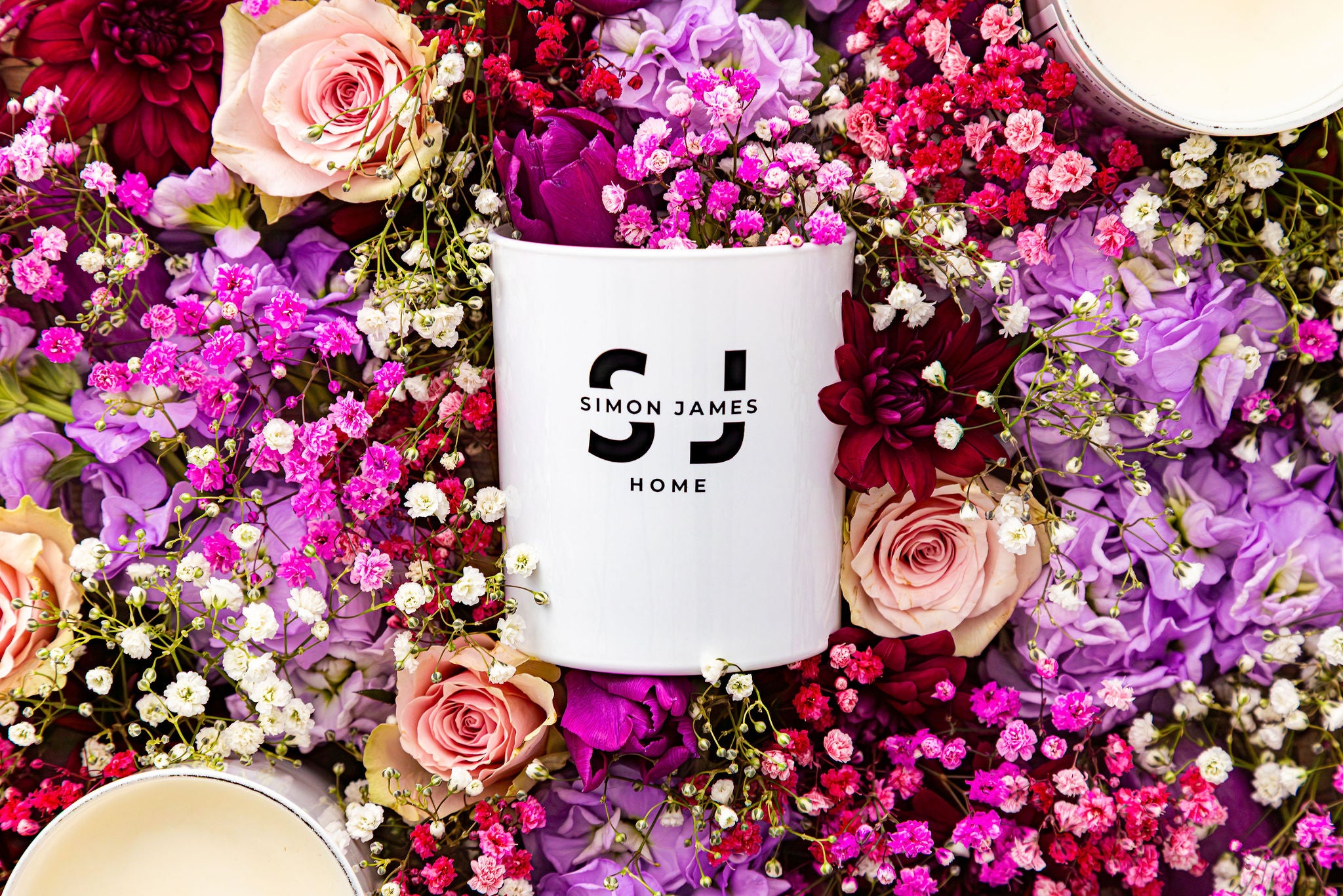 White candle with 'Simon James Home' logo surrounded by colorful flowers